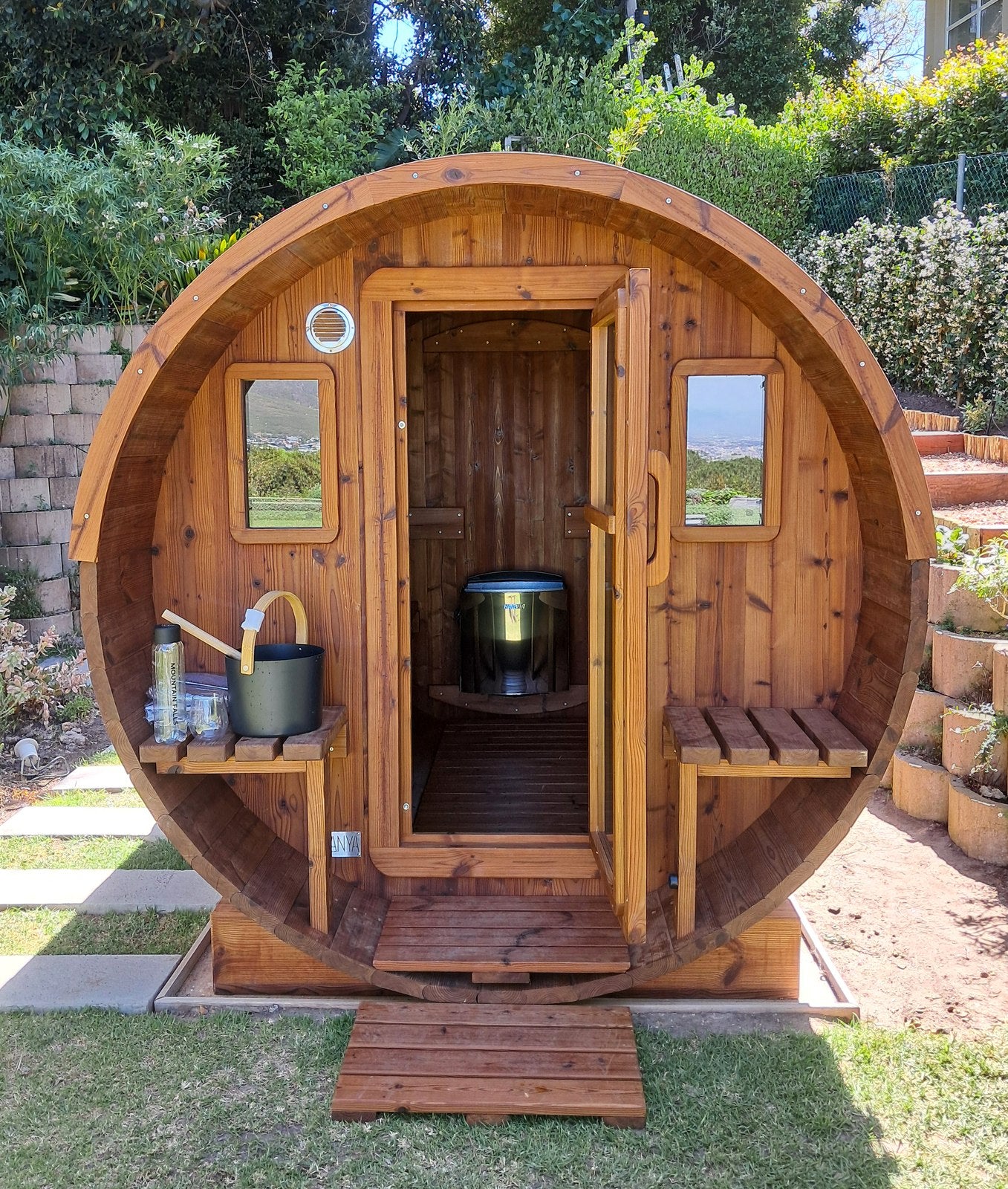 A BANYA barrel sauna lit by lanterns at dusk, a chair pulled up outside